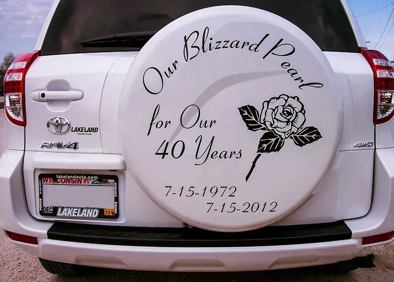 A white car with a tire cover that says our blizzard pearl for our 40 years