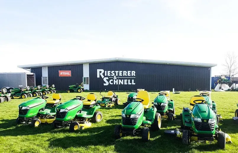 A row of green lawn mowers are parked in front of a building.