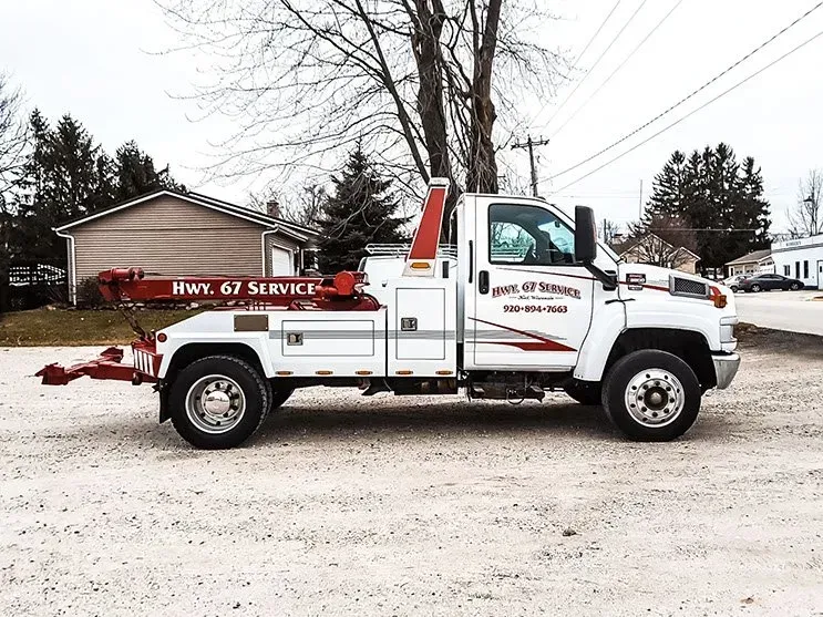 A white tow truck is parked in the dirt in front of a house.