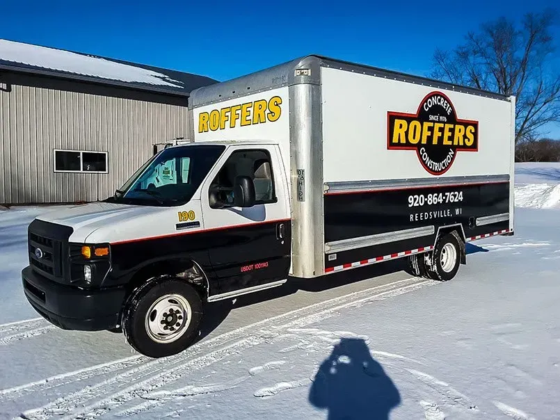 A rotters truck is parked in the snow in front of a building