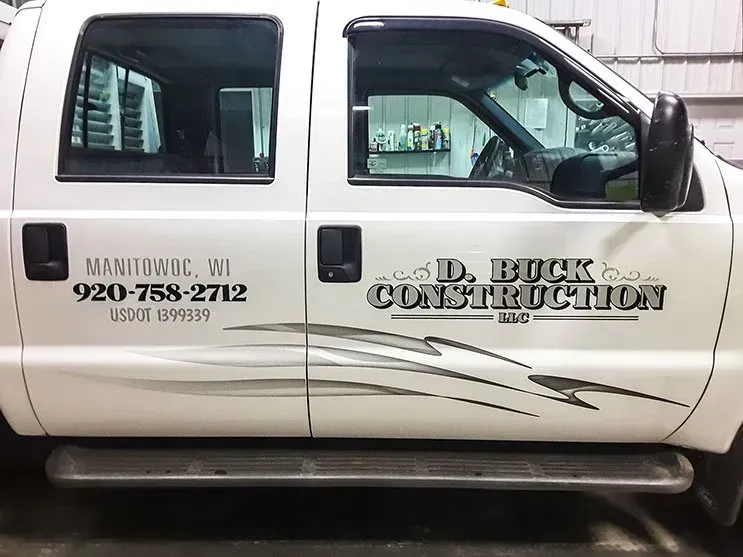 A white truck with the name d. buck construction on the side is parked in a garage.