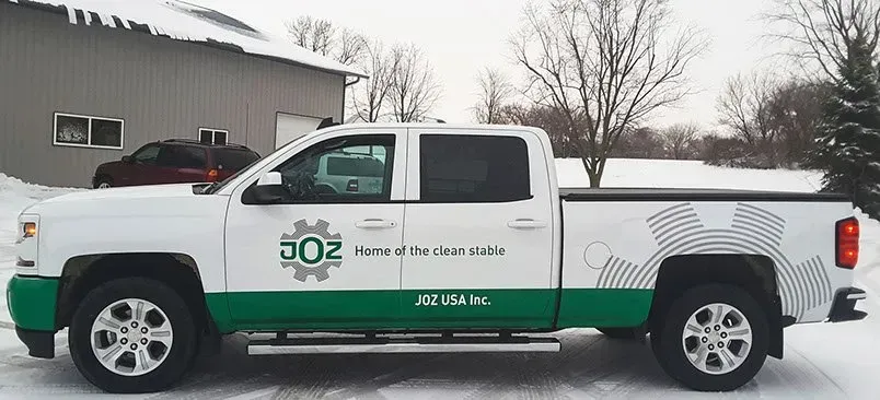 A white and green truck is parked in the snow in front of a building.