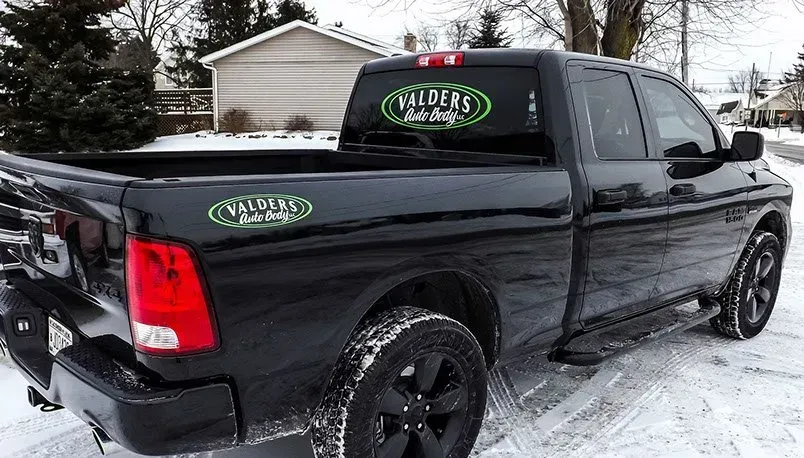 A black truck is parked in the snow in front of a house.