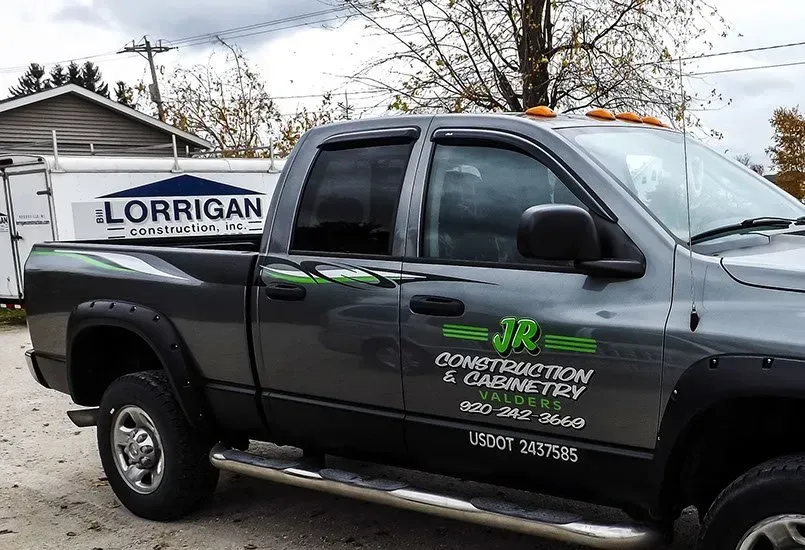 A lorrigan construction and cabinetry truck is parked in front of a building.