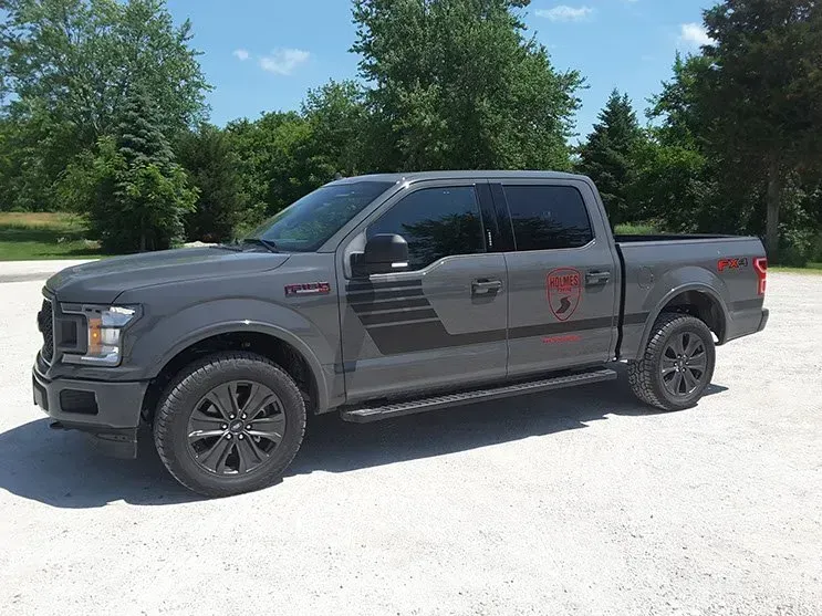 A gray ford f150 truck is parked in a gravel lot.
