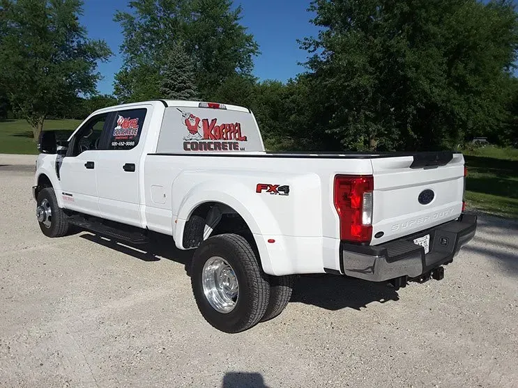 A white truck is parked in a parking lot with trees in the background.