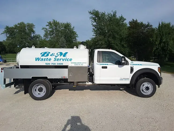 A white waste service truck is parked in a gravel lot