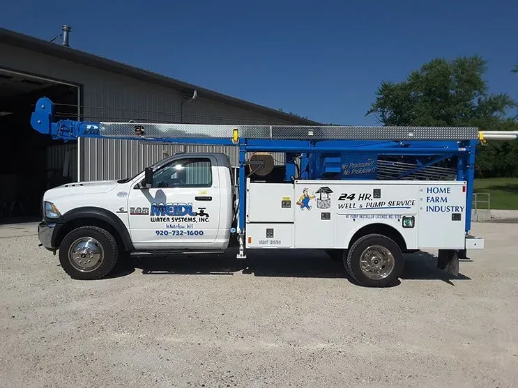 A white truck with a blue ladder is parked in front of a building.