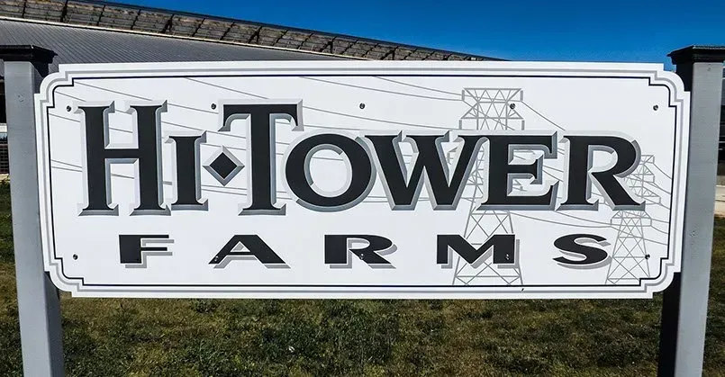 A sign for hi-tower farms is sitting in the grass.