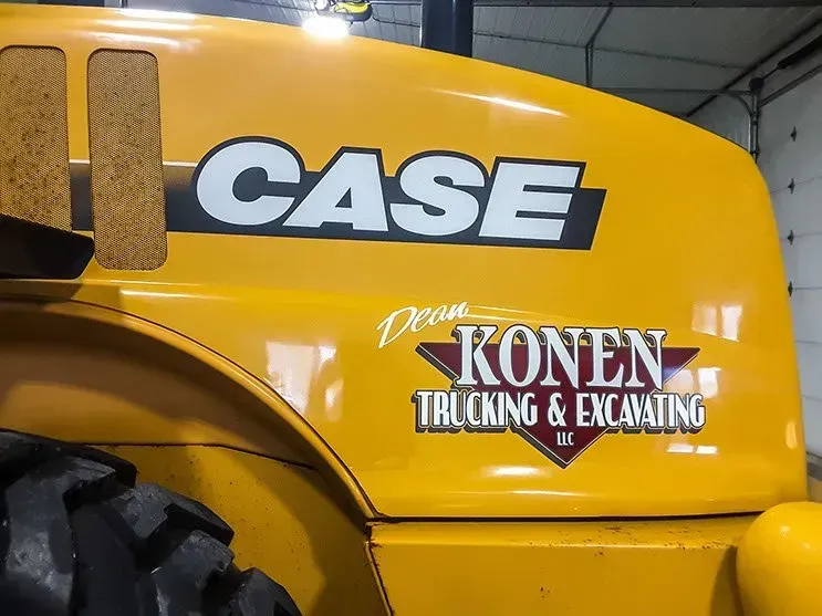 A yellow case truck with a konan trucking and excavating logo on the side