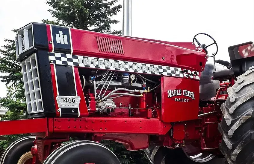 A red tractor is parked in front of a tree.