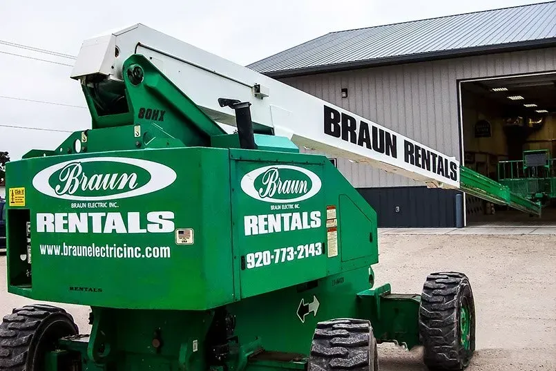 A green and white braun rentals lift is parked in front of a building