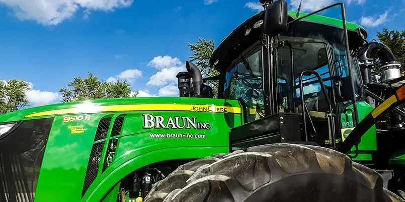 A green john deere tractor is parked in a field with trees in the background.