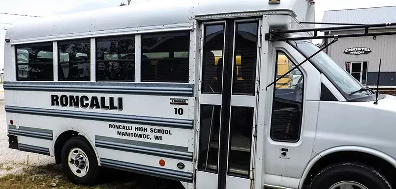 A white bus with the word roncalli on the side is parked in a field.