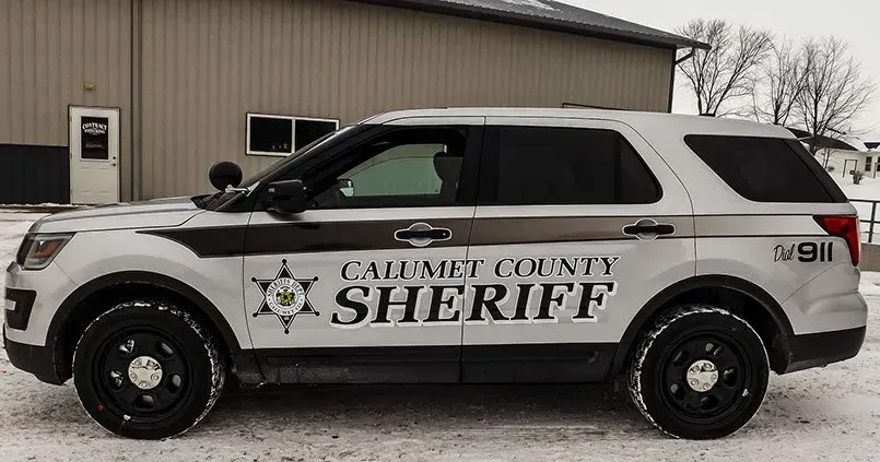 A sheriff 's car is parked in the snow in front of a building.