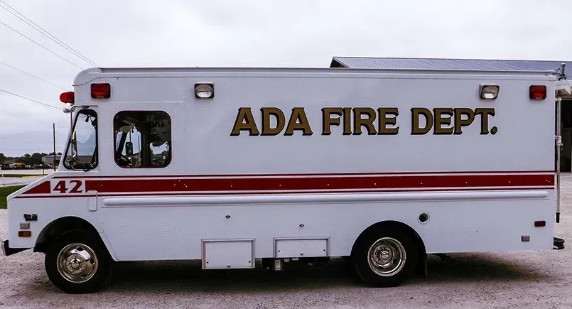 A white ambulance from the ada fire department is parked on the side of the road.