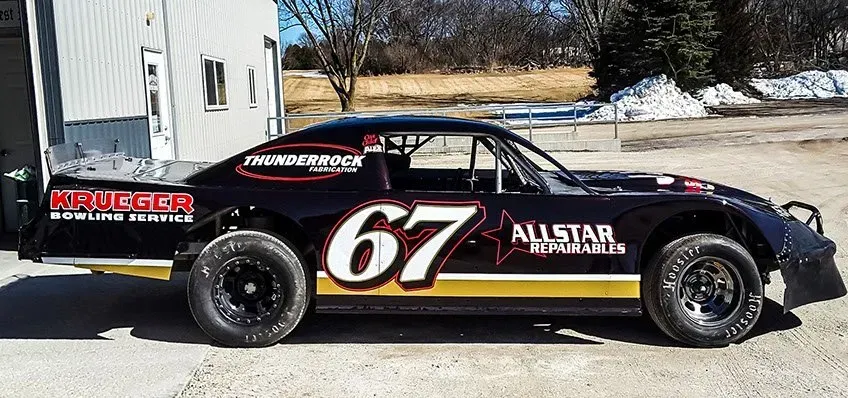 A race car with the number 67 on it is parked in a parking lot.