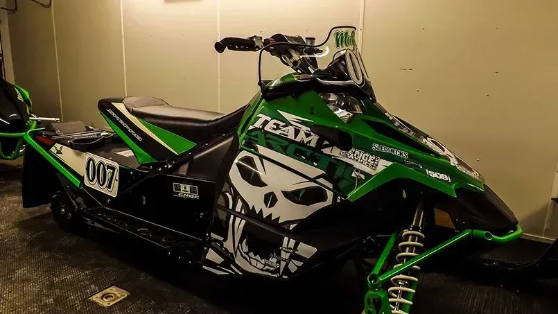 A green and black snowmobile with a skull on the side is parked in a garage.