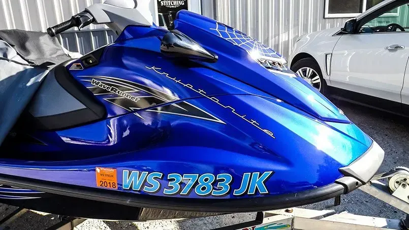 A blue jet ski with a license plate that says ws3783 jk is parked next to a white car.