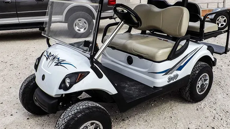 A white golf cart is parked in a gravel lot next to a truck.