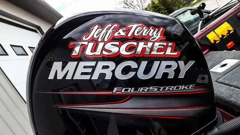 A mercury four stroke engine is sitting in front of a garage.