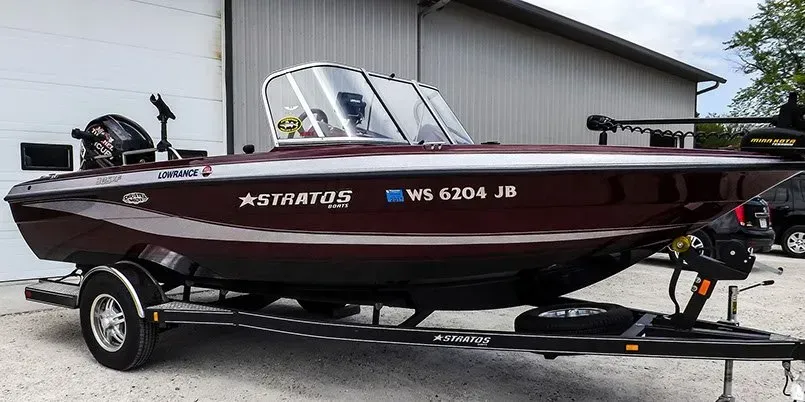 A fishing boat is parked on a trailer in front of a garage.