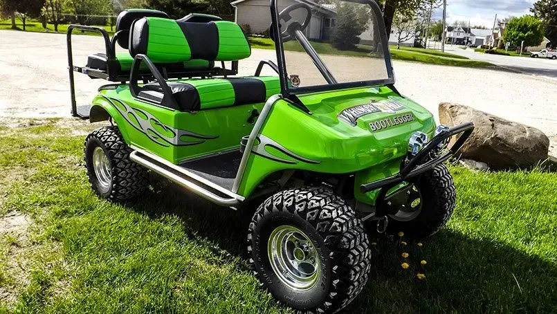 A green and black golf cart is parked in the grass.