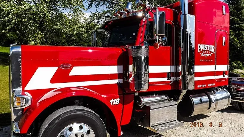 A red semi truck with white stripes on the side is parked in a gravel lot.