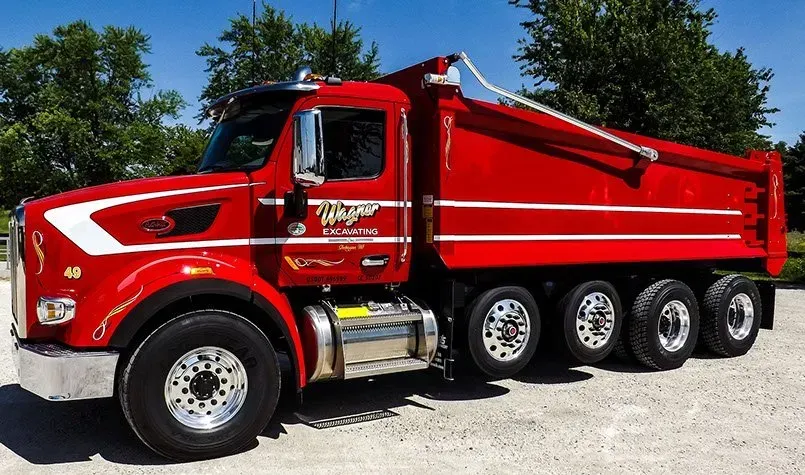 A red dump truck is parked in a gravel lot