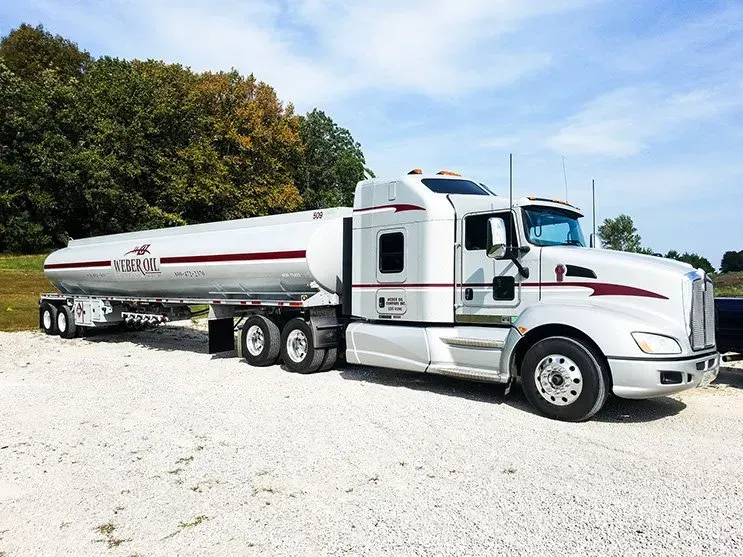 A white semi truck with a tanker trailer is parked in a gravel lot.