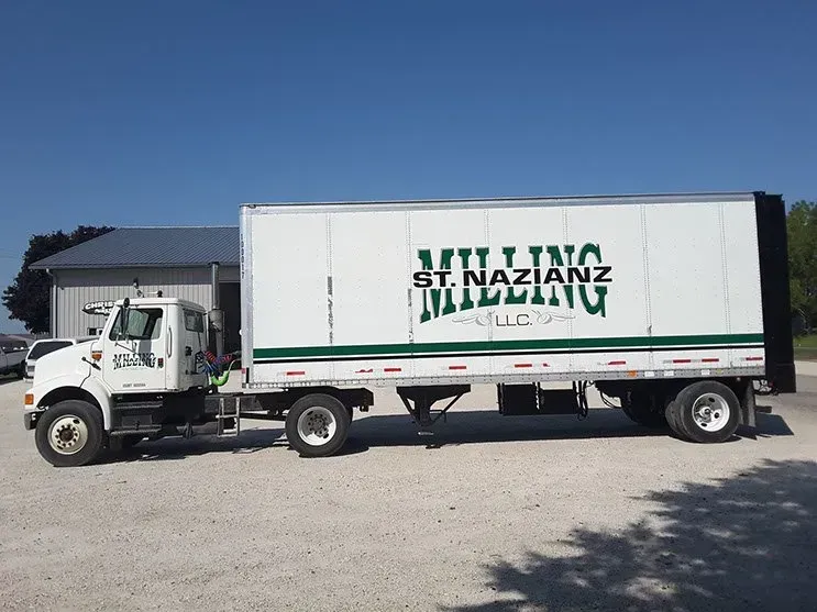 A white truck is parked next to a trailer that says st. nazianz building
