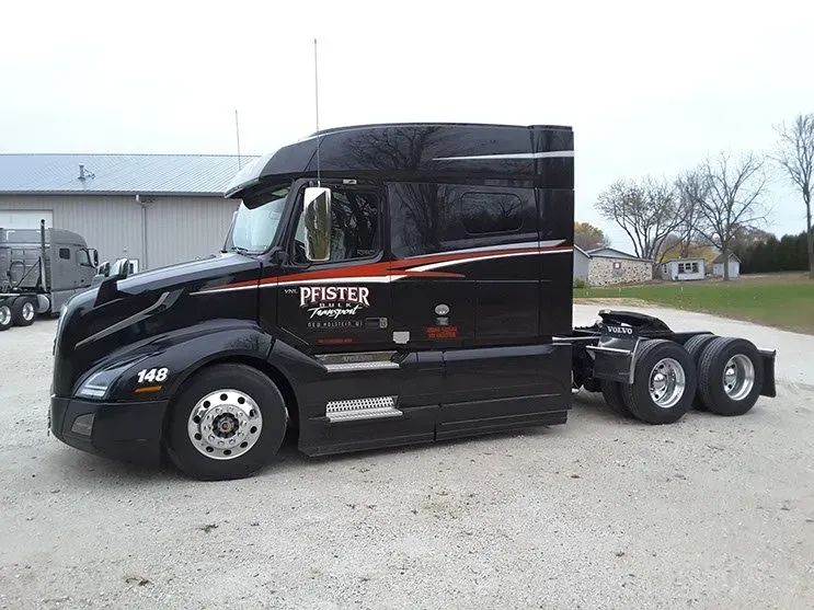 A black semi truck is parked in a gravel lot.
