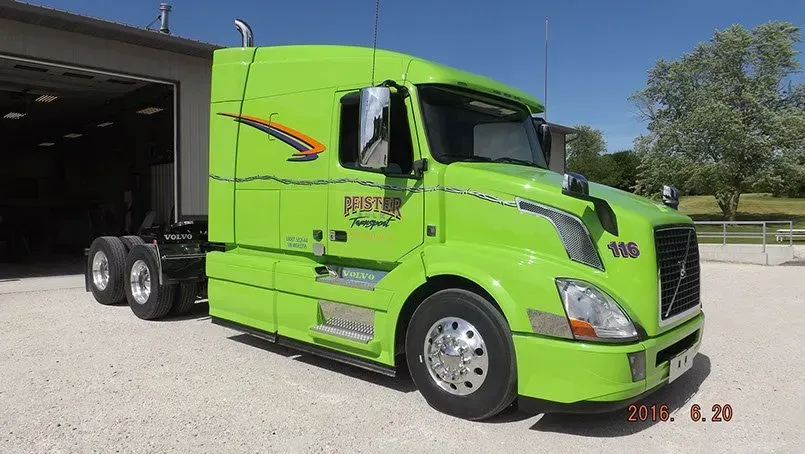 A green semi truck is parked in front of a garage.