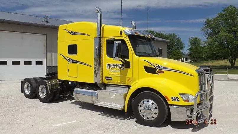 A yellow semi truck is parked in front of a garage.