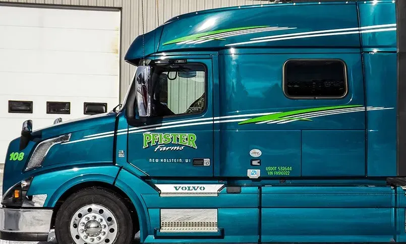 A blue semi truck is parked in front of a garage door.