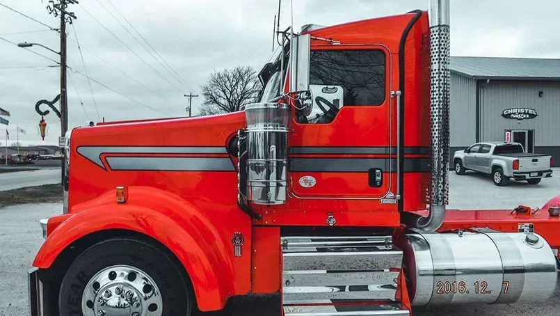 A red semi truck is parked in front of a building.