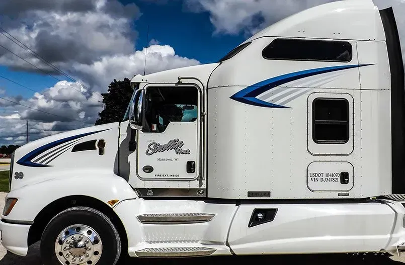 A white semi truck with blue stripes on the side is parked on the side of the road.