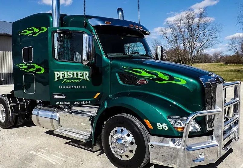 A green semi truck with the word pfister on the side is parked in a parking lot.