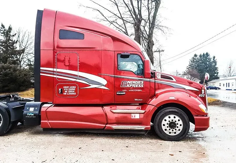 A red semi truck is parked in a gravel lot.