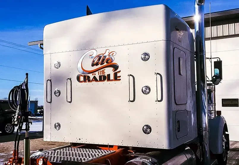 A white cradle semi truck is parked in front of a building.