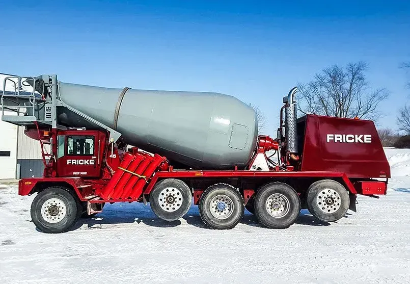 A red and gray concrete mixer truck is parked in the snow.