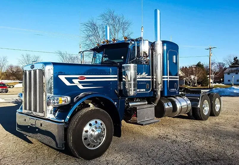 A blue semi truck is parked in a gravel lot.