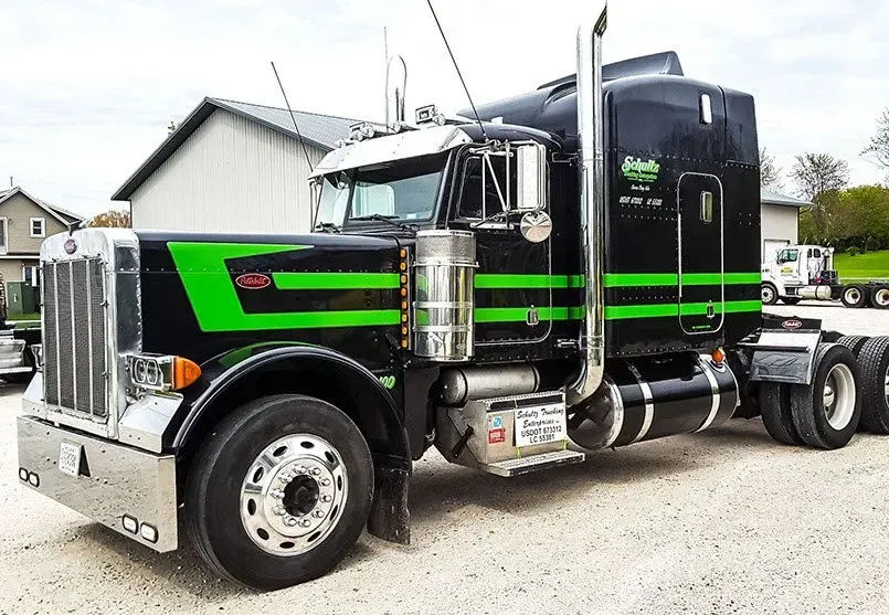 A black semi truck with green stripes on the side is parked in a gravel lot.