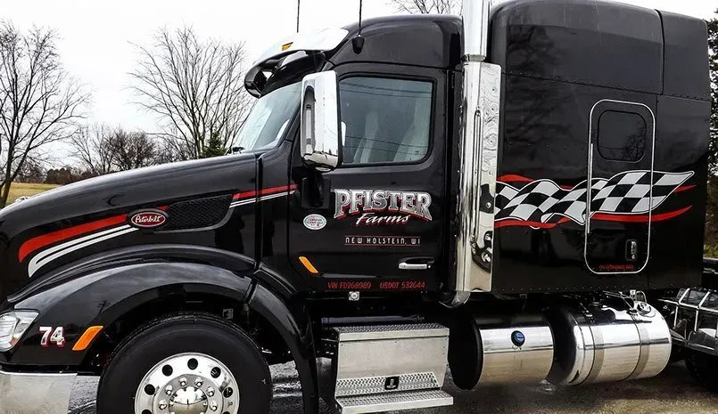 A black semi truck with a checkered pattern on the side is parked in a parking lot.