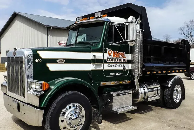 A green and white dump truck is parked in front of a building.