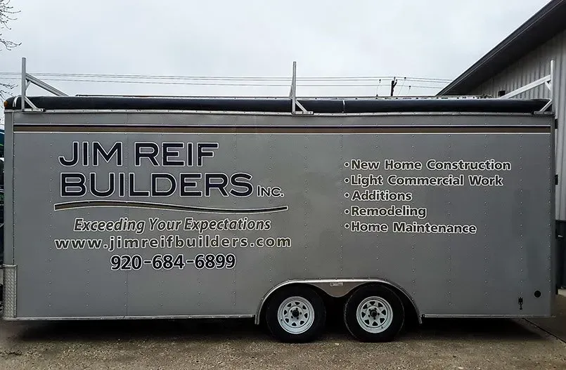A trailer for jim reef builders is parked in front of a building.