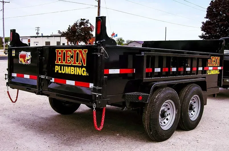 A hein plumbing dump trailer is parked in a parking lot