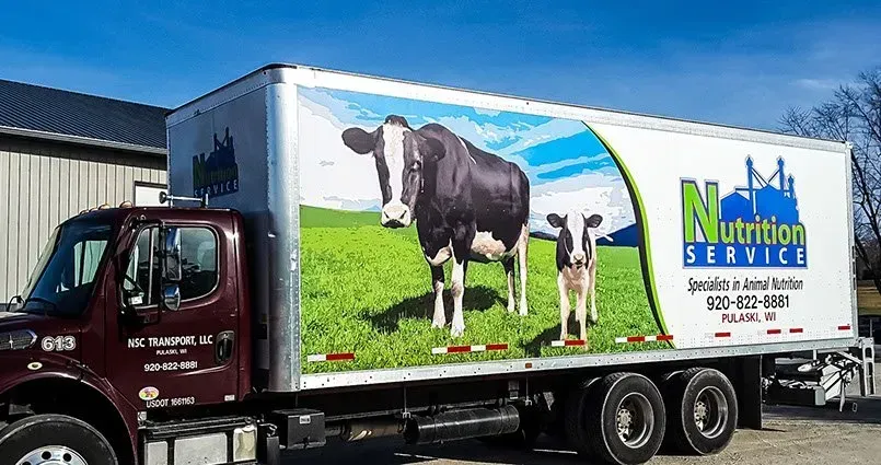 A truck with a picture of two cows on the side is parked in front of a building.