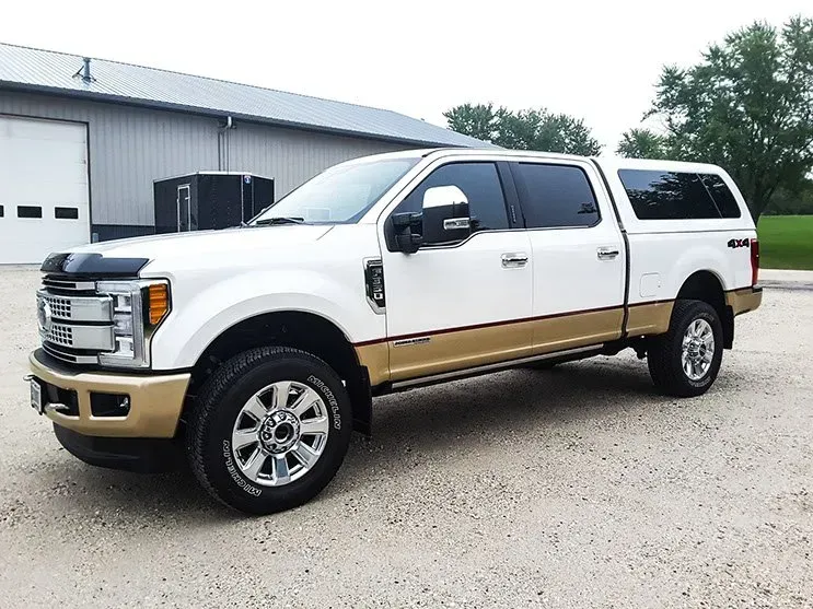 A white and gold pickup truck is parked in front of a building.