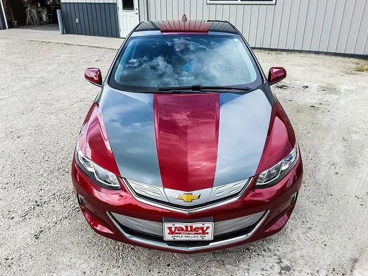 A red car with a valley license plate is parked in front of a building